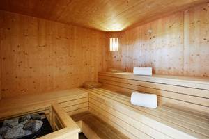Innenansicht einer Holzsauna mit braunen Holzwänden, Bänken und weißen Handtüchern