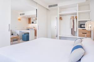 Innenansicht eines Zimmers im Carema Beach Menorca Hotel mit Bett, Kleiderschrank und Miniküche.