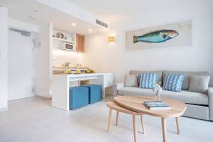 Wohnbereich des Carema Beach Menorca Hotels mit grauer Couch, blauen Kissen und einem Tisch.