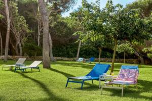 Gartenbereich des Victoria Menorca Hotels mit mehreren blauen und weißen Liegen auf grünem Rasen.