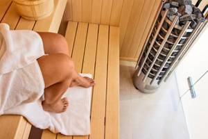 Person in einer Holzsauna im Victoria Menorca Hotel mit einem Holzeimer und einem vollen Kohlebecken.