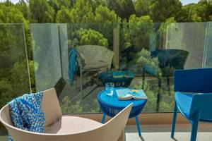 Balkon mit Aussicht auf Wald, blauen Stühlen und einem runden Tisch mit Buch