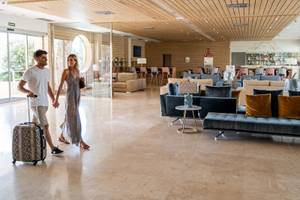 Ein Paar im Eingangsbereich des Seth 55 Santo Tomás Hotels, beide tragen Lächeln, während sie sich mit Gepäck durch die geräumige Lobby bewegen.