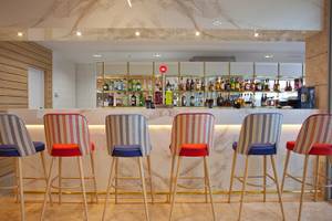 Innenansicht der Bar des Hotels Seth 55 Santo Tomás mit sechs bunten Barhockern und einer Theke mit vielen alkoholischen Getränken.
