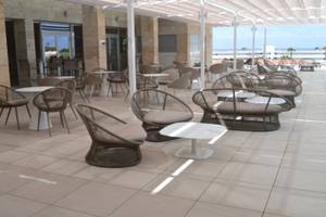 Hotelterrasse mit Tischen und Stühlen unter einem Sonnendach im Freien.