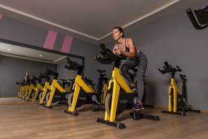 Eine Frau trainiert auf einem schwarzen und gelben Fahrrad im Fitnessstudio.