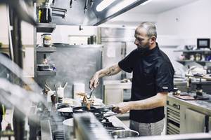 Ein Koch in einer professionellen Küche, der Garnelen auf einem Grillpfännchen brät.