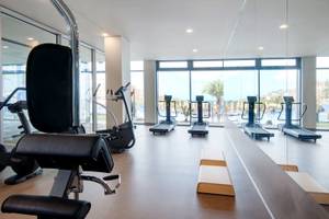 Fitnessbereich des Baia Azul Hotels mit modernen Geräten und großen Fenstern.
