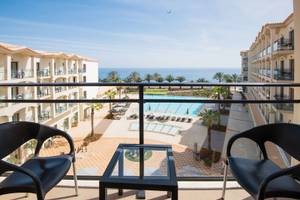 Blick vom Balkon auf das Meer beim Hotel Vila Galé Santa Cruz mit Swimmingpool und Gebäuden im Hintergrund.