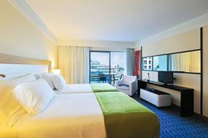 Zwei Betten mit weißem und grünem Überwurf in einem Hotelzimmer mit Stadtblick.
