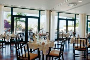 Innenansicht des Restaurants im Madeira Panorâmico Hotel mit vielen gedeckten Tischen und Fenstern.
