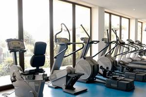 Fitnessgeräte im Hotel Porto Mare - PortoBay, in einer Reihe aufgestellt und vor großen Fenstern.