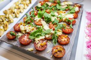 Gegrillte Tomaten mit Käse und Rucola auf einem Holzbrett serviert