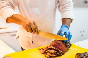 Koch schneidet Fleisch auf einem gelben Schneidebrett im Views Oasis Hotel