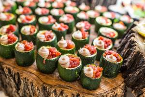 Nahaufnahme von grünen Zucchini-Tarteletts gefüllt mit einer roten Tomatenfüllung auf einem Holztisch.