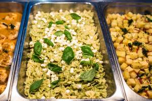 Buffet-Tisch mit verschiedenen Gerichten vom Views Oasis Hotel, darunter gebratenes Hähnchen, grüne Pasta mit Feta und Spinat sowie Kartoffelbeilage.