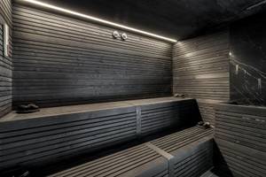 Innenansicht der Sauna im Royal Savoy Hotel mit schwarzen Holzwänden und Bänken.