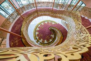Goldenes Spiraltreppenhaus im Savoy Palace Hotel mit rotem Teppich und kunstvollen Geländer