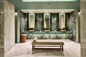 Badezimmer im Savoy Palace mit tropischen Tapeten, drei Waschbecken und Spiegeln, einer Bank und Marmorböden.