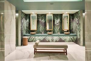 Badezimmer des Savoy Palace mit grüner Palmblatt-Tapete und drei Waschbecken.