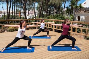 Drei Frauen machen Yoga auf einem Holzdeck im Freien.