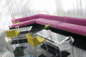 Hotelloungebereich mit einem großen pinken Sofa und gelben und durchsichtigen Stühlen vor einem Glastisch.