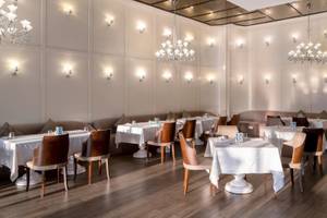 Innenansicht des Rixos Premium Belek Restaurants mit weißen Tischen, Holzboden und Kronleuchtern.