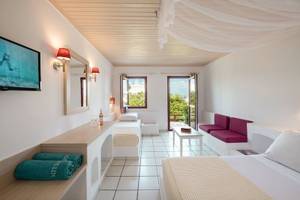 Innenansicht eines hellen Hotelzimmers im Mitsis Cretan Village Hotel mit zwei Betten, einem Fernseher und einer Terrasse.