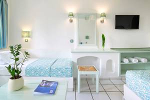 Innenansicht eines Zimmers im Mitsis Cretan Village Hotel mit zwei Betten, einem Fernseher und einem Tisch.