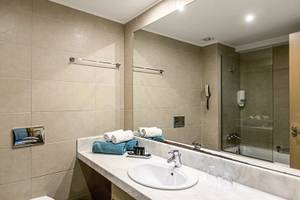 Badezimmer im Asterias Beach Resort mit Waschbecken, Spiegel und Duschbereich.