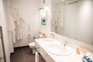 Badezimmer im Desert Rose Resort mit weißem Waschbecken, Spiegel und Robes an der Wand.