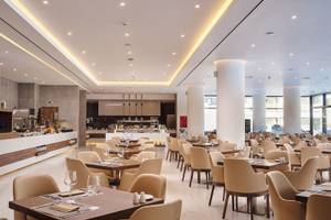 Innenansicht des Restaurants im Lindos Grand Resort & Spa mit leeren Tischen und Stühlen.