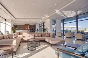 Lobby des Lindos Grand Resort & Spa mit weißen Wänden, großen Fenstern und modernen Möbeln.