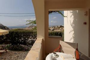 Blick vom Balkon des Proteas Hotel & Suites auf eine begrünte Terrasse mit einer offenen Buch und einer Tasse Kaffee.