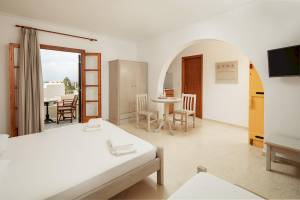 Innenansicht eines Zimmers im Proteas Hotel & Suites mit zwei Betten, Tisch, Stühlen und einem offenen Balkon.