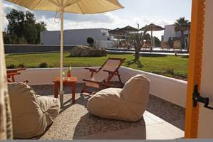 Außenbereich des Aegean Palace Hotels mit Loungestühlen, Kissen und Sonnenschirmen auf der Terrasse.