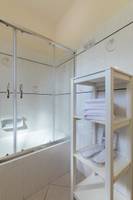 Badezimmer mit einer Dusche und einem Schrank, der Handtücher und Hausschuhe bereithält.