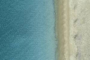 Luftaufnahme von kristallklarem Wasser und sandigem Strand, die sich treffen.
