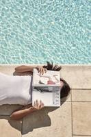Eine Frau liegt am Pool und liest ein Magazin.