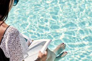 Frau sitzt im Schwimmbad und liest ein Buch