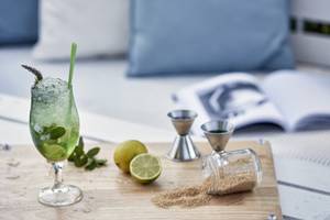 Ein grüner Cocktail mit Minze und Limette auf einem Holzschneidebrett.