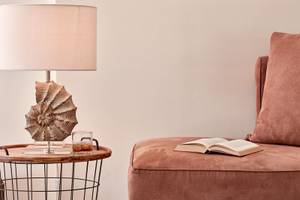 Ein Stuhl mit einem Buch und einem Glas auf einem Tisch neben einer Lampe.