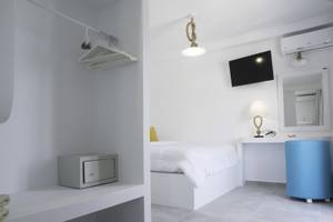 Innenansicht eines Zimmers im Amaryllis Paros Beach Hotel mit weißem Bett, Schreibtisch und blauem Stuhl.