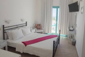 Ein Schlafzimmer im Amaryllis Paros Beach Hotel mit einem Doppelbett, weißem Bettzeug und einem roten Schal.
