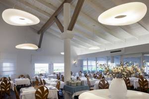 Restaurantbereich des Mare Pineta Hotels mit weißen Tischen und Stühlen, Holzdecken und großen Hängelampen.