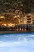 Ein Hotelpool und Bar mit Steinwänden und beleuchteten Tischen und Stühlen.