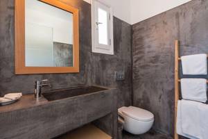 Badezimmer im Paros Agnanti Resort & Spa mit grauen Wänden, einem Waschbecken, einer Toilette und Handtüchern.