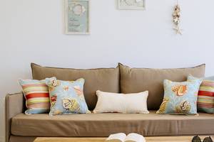 Wohnzimmer mit einem braunen Sofa, verschiedenen gemusterten Kissen und einem offenen Buch auf einem Tisch.