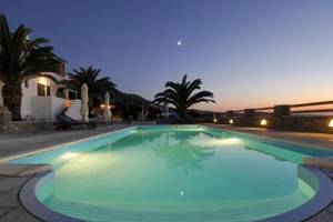 Ein Swimmingpool im Garten des Pyrgaki Hotels bei Nacht, beleuchtet und umgeben von Palmen und Sonnenliegen.