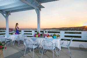 Terrasse des Pyrgaki Hotels mit Blick auf den Sonnenuntergang und mehreren gedeckten Tischen.